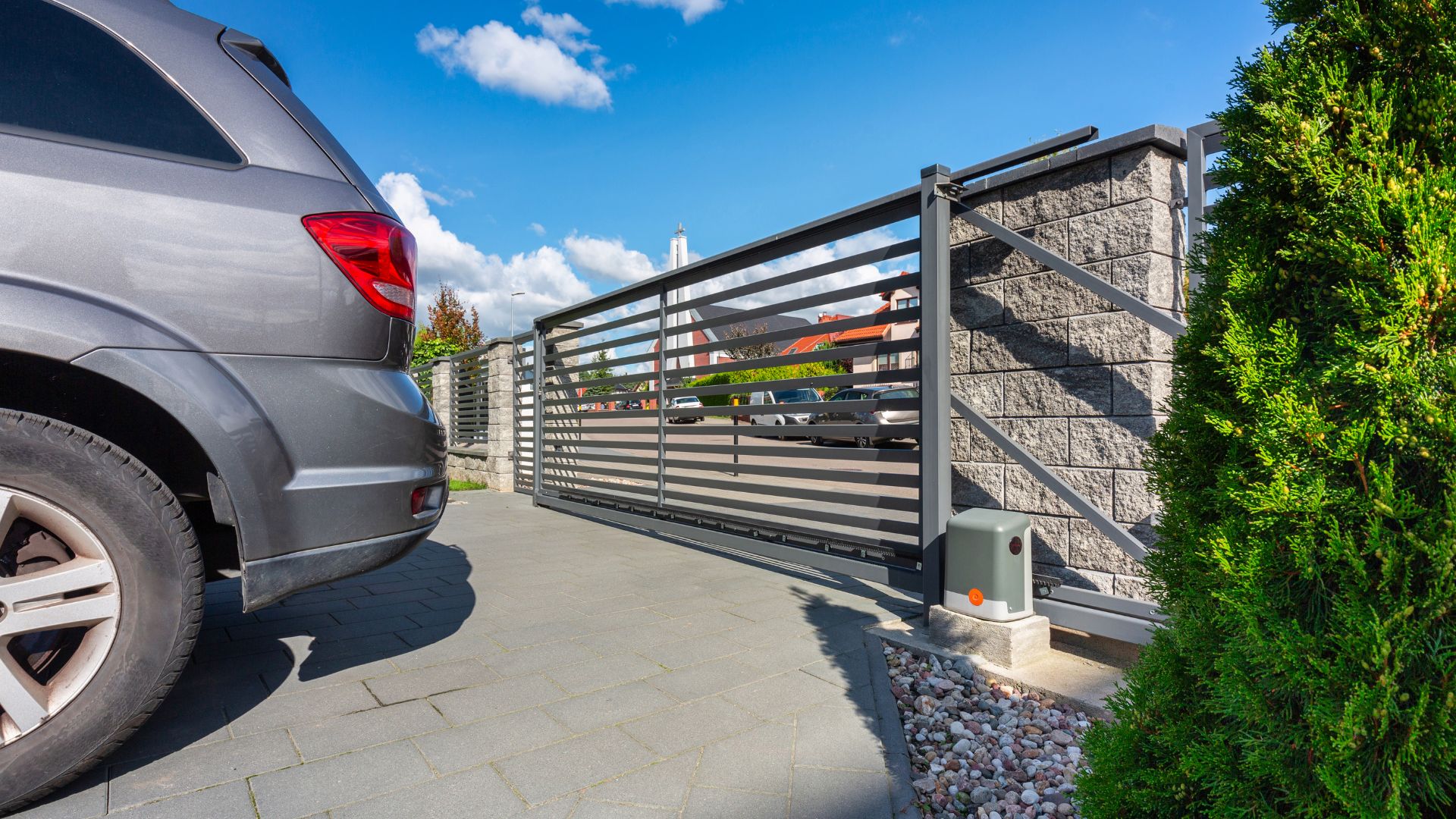 Automatic sliding gate with car entrance and stone wall on sunny day