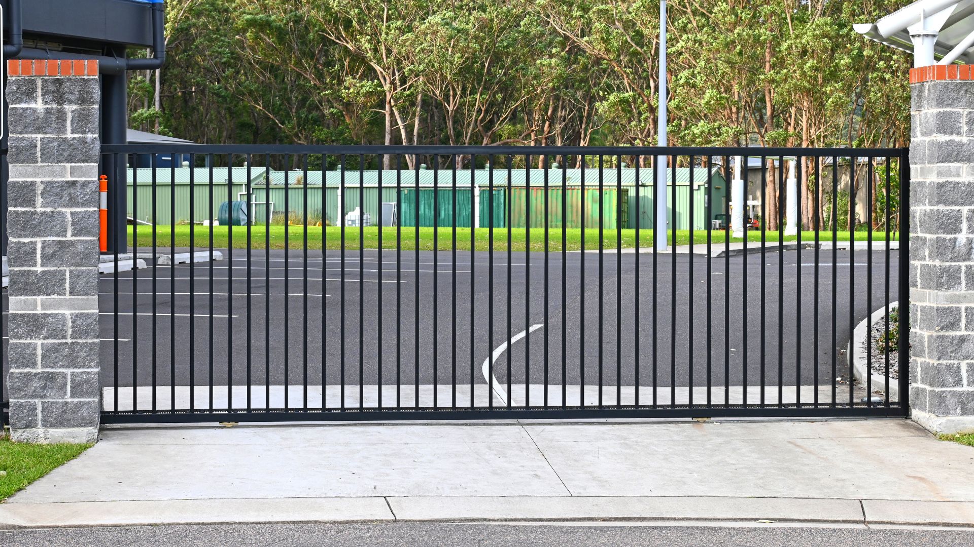 Closed black metal sliding gate between brick walls with trees in background